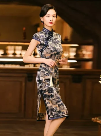 Elegant model wearing a misty blue bamboo pattern print brocade cheongsam dress, holding a traditional hand fan, standing in a vintage bar setting to showcase the dress's mandarin collar, frog buttons, and high slit.