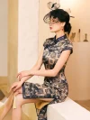 Woman sitting in a misty blue bamboo print brocade cheongsam dress with a high slit, wearing a polka dot birdcage veil hat, showcasing the dress's fit and side details against a minimalist background.