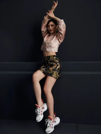 Full-body fashion shot of the misty pink modernized jacquard short qipao top, featuring traditional frog buttons, high mandarin collar, and delicate wave jacquard pattern; paired with a tiger print mini skirt and sneakers for a trendy modern cheongsam top look