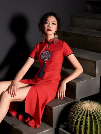 Woman model sitting on concrete stairs wearing a red vintage cheongsam dress with embroidery tassel accent, showing the high slit design and elegant silhouette.