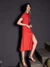 Woman model in walking pose showing the high slit design of a red modified cheongsam dress with traditional embroidery and tassel, modern vintage aesthetic.