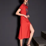Woman model in walking pose showing the high slit design of a red modified cheongsam dress with traditional embroidery and tassel, modern vintage aesthetic.