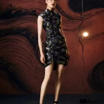 Full-body studio shot of model in form-fitting ink black modern Chinese silk mini cheongsam dress, featuring a high front slit, tailored silhouette, and elegant styling with strappy heels.