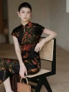 Elegant woman seated in a minimalist neutral toned room, wearing a modern Chinese mulberry silk slim fit qipao dress with delicate lychee and butterfly print. This high end lightweight short sleeve cheongsam blends vintage charm with modern aesthetics.