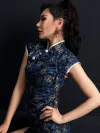 Close-up side profile view of a woman wearing a modern fashion dark blue peacock short cheongsam, showcasing the intricate peacock print, traditional mandarin collar, silver frog buttons, and elegant silhouette of this dark blue cheongsam.