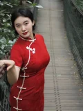 Plus size model posing on a forest suspension bridge in a modern red midi qipao, featuring delicate white floral frog buttons and a tailored silhouette. This contemporary red qipao blends classic Chinese details with everyday wearability.