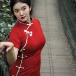Plus size model posing on a forest suspension bridge in a modern red midi qipao, featuring delicate white floral frog buttons and a tailored silhouette. This contemporary red qipao blends classic Chinese details with everyday wearability.