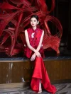 Modern Red Silk Qipao Set - Full-body shot of woman in two-piece red qipao set, featuring a sleeveless brocade top and flowing satin skirt, sitting in front of a red bamboo art installation, ideal modern red qipao for formal occasions