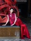 Modern Red Silk Qipao Set - Woman reclining on a black marble countertop in a two-piece red qipao set, featuring floral brocade top and wide-leg satin bottom, with a red bamboo art installation backdrop