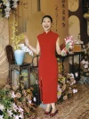 Modern Red Silk Wedding Cheongsam - Bride in red silk cheongsam waving joyfully at a wedding reception, wearing form-fitting sleeveless qipao with mandarin collar and side slit, surrounded by floral decor, elegant cheongsam for wedding celebrations.