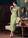 Woman in a mulberry silk green cheongsam dress with delicate magnolia print, standing with crossed legs while holding a teacup, showcasing the dress's flowing fabric and elegant retro charm.