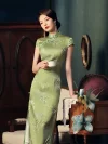 Elegant woman holding a white teacup, wearing a mulberry silk green slim fit long cheongsam dress with magnolia print, posing in a vintage-style room to show the smooth fabric and traditional mandarin collar.