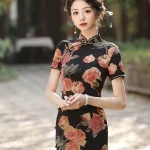 Front view of women's Old Shanghai peony pattern short sleeve cheongsam (qipao) with black base and vintage rose print, model standing outdoors with hands clasped, featuring elegant stand-up collar and traditional frog buttons.