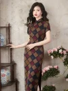 Old Shanghai style checkered cheongsam for women, a full length high slit qipao with short sleeves. The vintage plaid pattern in earthy tones is showcased as the model stands by a wooden shelf with traditional vases and floral decor in the background.