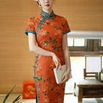 Vintage Old Shanghai style long cheongsam (qipao) in tangerine red with peony floral print and blue trim, elegant women's traditional Chinese dress, model holding a book.