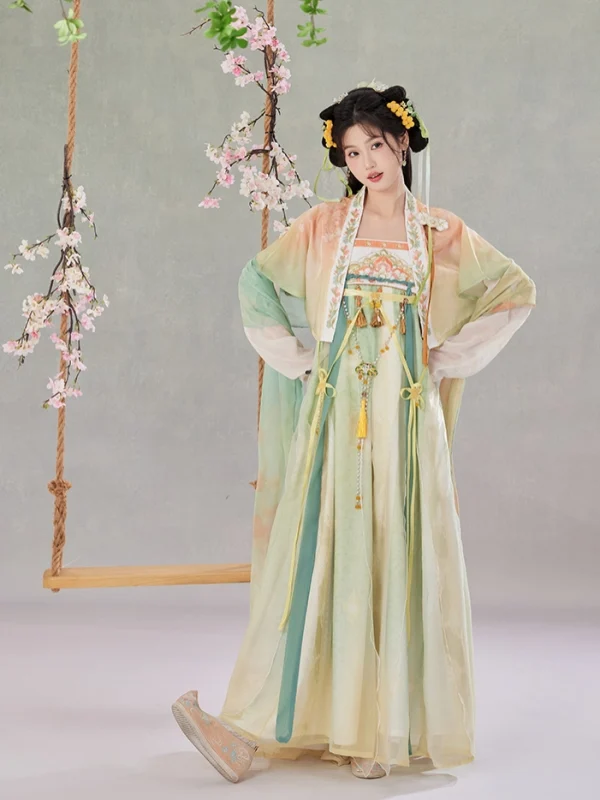 Young woman wearing soft green-yellow gradient waist-length ruqun hanfu, elegant Tang-style traditional Chinese clothing with sheer embroidered sleeves, styled with floral hair ornaments in a studio setting with cherry blossom swing decor.