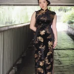 Full-body styled look of the black chinese cheongsam dress, a Chinese Black Sleeveless Plus Size Long Daily Cheongsam with classic gold bamboo and fan motifs. This qipao black dress is paired with modern accessories, showcasing its versatility as a daily wear piece for plus size women.