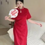 Plus size model wearing a vibrant red satin qipao dress, elegant chinese red qipao with pearl-trimmed mandarin collar and keyhole neckline, posing with a wedding fan in a warm modern home setting.