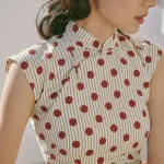 Close-up detail of a cotton qipao dress showing the traditional handcrafted frog button and polka dot-stripe print on premium fabric.