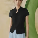 Full front view of a black modern qipao top, a versatile qipao inspired top with mandarin collar and traditional frog buttons, worn by a model in a minimalist studio.