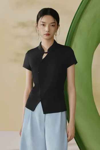 Full front view of a black modern qipao top, a versatile qipao inspired top with mandarin collar and traditional frog buttons, worn by a model in a minimalist studio.