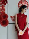 Red Chinese Cheongsam Dress - Close-up shot of bride in 2 piece cheongsam set, wearing textured red mandarin collar vest with floral buttons, holding a pink flower in front of a wall decorated with red wedding ornaments, elegant bridal cheongsam.