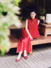 Red Chinese Cheongsam Dress - Bride in 2 piece cheongsam sitting on a wooden outdoor terrace, wearing textured red sleeveless top and flowing maxi skirt with red ballet flats, modern bridal cheongsam for outdoor wedding photos.