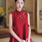 2 Piece Red Chinese Cheongsam Dress - Woman in elegant two-piece cheongsam set with sleeveless mandarin collar vest and matching skirt, sitting in a traditional Chinese room with ink painting screen backdrop, modern red cheongsam for formal events.