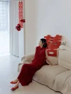 Red Chinese Cheongsam Dress - Bride in elegant 2 piece cheongsam set with textured sleeveless mandarin collar vest and matching maxi skirt, sitting on a sofa in a minimalist wedding prep room decorated with red double happiness signs, modern bridal cheongsam for engagement photos.