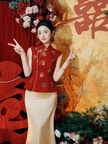 2 Piece Red and Gold Qipao Bridal Outfit - Bride in sequined red and gold qipao top with floral embroidery, paired with cream satin maxi skirt, posing playfully at wedding backdrop with red decor