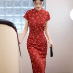 Elegant woman walking down stairs in a red base fresh floral slim fit long qipao, showcasing the form-fitting silhouette and traditional mandarin collar in a bright indoor setting.
