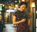 Woman wearing elegant red and black lace cheongsam dress, holding a decorated folding fan in a warm neon-lit vintage night Shanghai street, embodying classic 1930s Chinese qipao glamour.