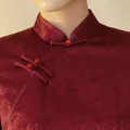 Close-up detail shot of women's red rose print cheongsam dress, focusing on the traditional mandarin collar, red frog buttons, and smooth jacquard fabric texture of this retro prom cheongsam.