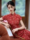 Close-up shot of a model in a red floral Chinese qipao dress, leaning on a sofa and holding a pink lily, highlighting the fabric texture and the dress's mandarin collar and buttons.