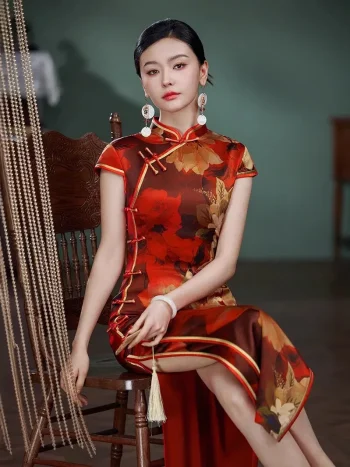 Close-up of a woman in a red silk qipao with vibrant floral print, sitting on a carved wooden chair to highlight the traditional frog buttons, mandarin collar, and smooth mulberry silk texture.