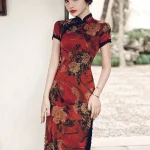 Close-up shot of a woman wearing a red floral vintage silk qipao dress, leaning against a white wall to showcase the peony print fabric, mandarin collar, and short sleeves.