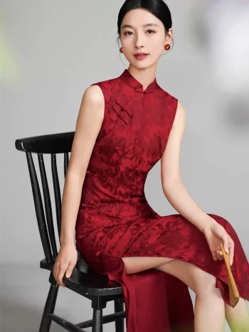 Woman in a deep red floral jacquard sleeveless chinese qipao, vintage-inspired long cheongsam dress sitting on a traditional wooden chair, elegant formal wear for weddings or events.