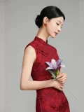 Side view of woman in red floral jacquard qipao, sleeveless vintage chinese cheongsam dress with traditional frog buttons, holding a lily flower in a minimalist studio setting.
