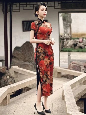 Profile view of a woman in a red floral vintage silk qipao dress standing on a stone bridge, highlighting the high side slit, lace trim, and traditional frog buttons along the placket.