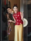 Red and Gold 2 Piece Qipao for Wedding - Bride in two-piece Chinese qipao with gold floral sequins, red sleeveless mandarin collar top and golden skirt, posing with groom behind door with double happiness decor