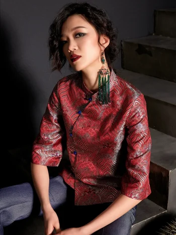 Close-up shot of a woman wearing the modern Chinese red jacquard satin cheongsam top, featuring intricate wave pattern, blue frog buttons, and high collar; paired with jeans for contemporary qipao top fashion