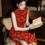 Red Modern Style Jacquard Sleeveless Cheongsam Dress - Woman sitting on a vintage upholstered armchair reading a book, wearing a red jacquard cheongsam with deep floral motifs. The sleeveless qipao features a form-fitting silhouette, side slit, and elegant mandarin collar, creating a retro literary aesthetic.