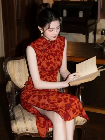 Red Modern Style Jacquard Sleeveless Cheongsam Dress - Woman sitting on a vintage upholstered armchair reading a book, wearing a red jacquard cheongsam with deep floral motifs. The sleeveless qipao features a form-fitting silhouette, side slit, and elegant mandarin collar, creating a retro literary aesthetic.