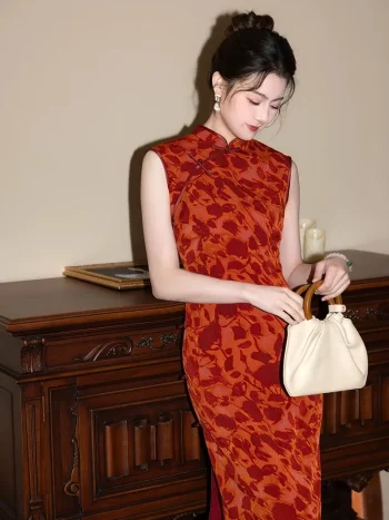 Red Modern Style Jacquard Sleeveless Cheongsam Dress - Close-up full-body shot of a woman in a red jacquard qipao with floral pattern, leaning against a vintage wooden cabinet. The sleeveless cheongsam showcases its high mandarin collar, traditional frog buttons, and textured fabric under soft warm lighting.