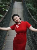 Full-body shot of a woman in a modern red qipao midi dress, standing with arms open on a wooden suspension bridge. The vibrant red hue and traditional trim highlight this plus size red qipao's timeless appeal.