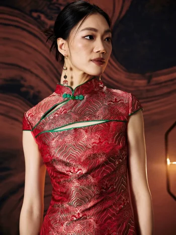 Model wearing a vibrant red modern design mini qipao dress, close-up view highlighting the green frog buttons, mandarin collar, chest cutout, and traditional wave brocade jacquard pattern on premium satin fabric.
