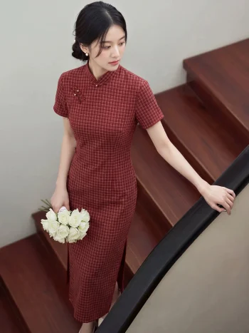 Women's 1940s traditional red plaid qipao, a classic red qipao dress with a refined checkered pattern, tailored fit, and vintage-inspired design. The model stands on a wooden staircase holding a bouquet of white roses, showcasing the flattering silhouette and elegant charm of this timeless traditional qipao.