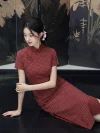 Close-up view of women's 1940s traditional red plaid qipao, featuring a classic checkered pattern, short sleeves, stand-up collar with frog buttons, and a flowing silhouette. The model sits on a dark floor indoors, highlighting the fabric texture and vintage details of this elegant red qipao.