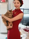 Women's Modified Chinese Red Qipao Dress - Bride in red qipao dress holding a cat during bridal prep, wearing sleeveless form-fitting chinese dress qipao with gold jewelry, warm indoor wedding scene
