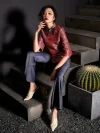 Full-body shot of a woman in the red jacquard satin cheongsam top sitting on concrete stairs, paired with flared jeans and mules; modern Chinese qipao top fashion with edgy styling